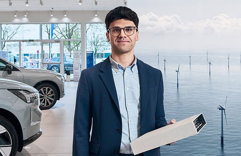 Mann hält Aktenordner. Im Hintergrund ist ein Autohaus und ein Offshore Windpark zu sehen.